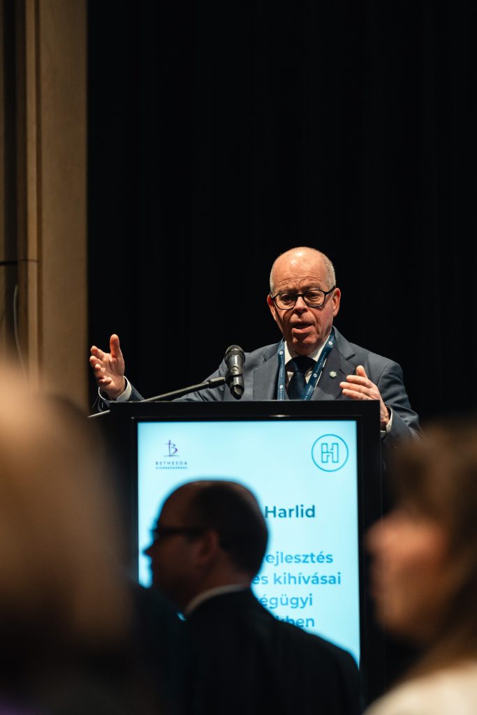 Férfi előadó tart szakmai előadást a konferencia pódiumán.